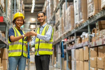 African American female worker and an Asian male worker wearing safety uniforms join hands together to serve in a wholesale warehouse.