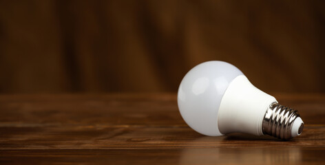 Light bulb on a brown wooden background. Saving energy, electricity, save power or energy crisis banner.