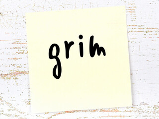 Yellow sticky note on wooden wall with handwritten word grim