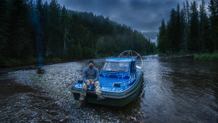 A man is sitting on an airboat. A guy on a boat on a river in the woods