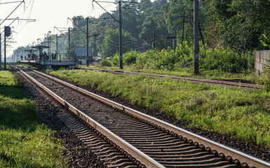Fototapeta na wymiar Suburban train waiting platform. Electrified railway tracks stretching into the distance. Selective focus.
