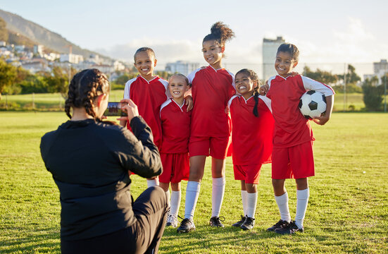 Soccer, photograph and sports coach with a girl team posing for a picture outdoor on a football field for fitness or training. Exercise, teamwork and picture with athlete kids or friends outside