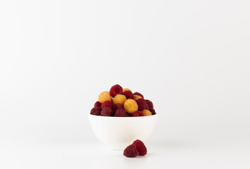 A pristine white bowl brimming with fresh, vibrant raspberries, set against a stark white background, highlighting nature's palette