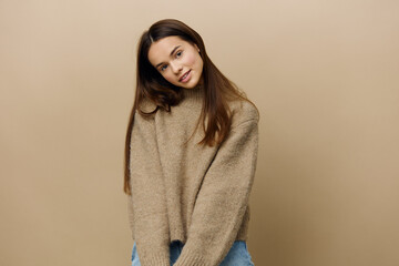 a sweet, modest, sophisticated woman stands on a beige background in a textured, warm sweater and looks at the camera with a sweet smile