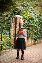 Little cute girl in witch costume holding jack-o-lantern pumpkin. Kid trick or treating in Halloween holiday.