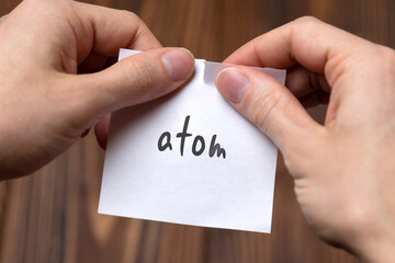 Hands tearing off paper with inscription atom