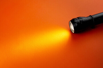 A bright beam of light from a flashlight shines on an orange background, Halloween theme copy space