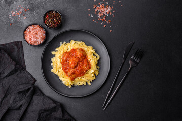 Pasta with beef meatballs in tomato sauce with spices and herbs on a dark background