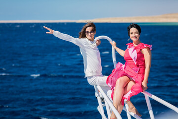 Two women relaxing together on the nose of the yacht at a sunny summer day at sea and enjoying at...