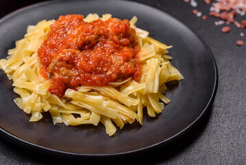 Pasta with beef meatballs in tomato sauce with spices and herbs on a dark background