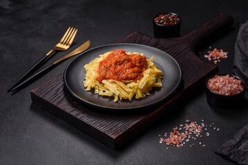 Pasta with beef meatballs in tomato sauce with spices and herbs on a dark background