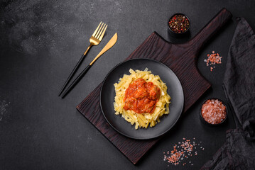 Pasta with beef meatballs in tomato sauce with spices and herbs on a dark background