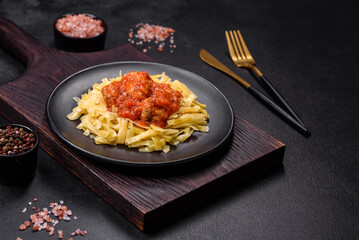 Pasta with beef meatballs in tomato sauce with spices and herbs on a dark background