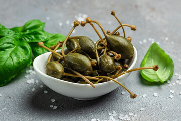 Capers. Marinated or pickled canned capers fruit with fresh basil leaves in a small bowl, on gray background. Long banner format. top view