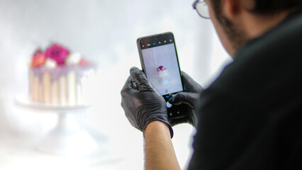 designer photographing frosted lilac romantic happy birthday cake on smartphone
