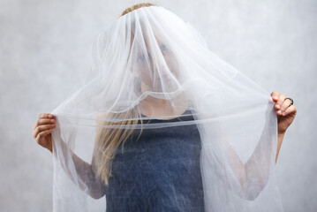 Child girl covers her face with a white veil