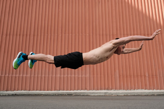 Side View Full Body Shot Of Strong Young Man Having Workout Outdoors Levitating In Horizontal Jump