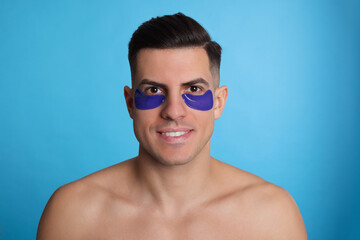 Fototapeta premium Man with under eye patches on light blue background
