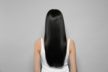 Young woman with long straight hair on grey background, back view
