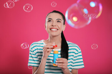 Young woman blowing soap bubbles on pink background