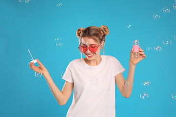 Young woman blowing soap bubbles on light blue background - Powered by Adobe