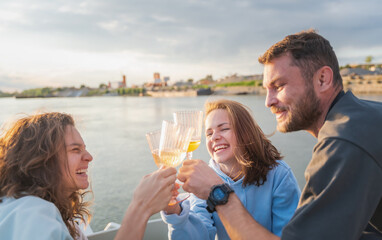 Group of happy young friends enjoying boat trip at sunset drinking wine and celebrating