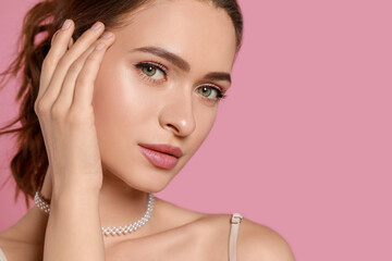 Young woman wearing elegant pearl necklace on pink background, closeup. Space for text