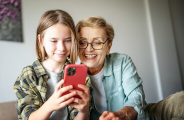 Smiling girl granddaughter with happy grandmother having fun and using looking at smartphone screen