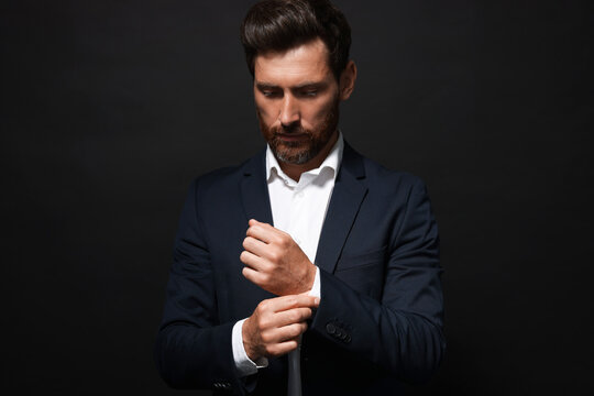 Handsome bearded man adjusting cufflinks on black background