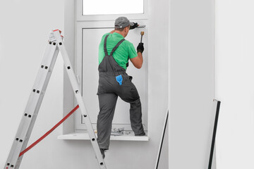 Worker in uniform installing double glazing window indoors, back view