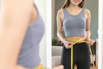 Young slim woman measuring her waist by measure tape after a diet