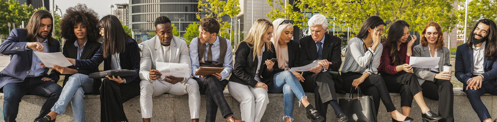 Diverse businessmen and businesswomen, sitting outside an office building taking a break together,...