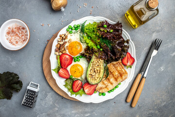 Plate with keto diet food. Keto breakfast Fried egg, avocado, strawberry, grilled chicken fillet, nuts and fresh salad, Ketogenic diet. Healthy food concept, top view