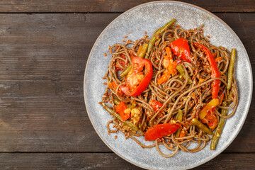 Soba with vegetables in soy sauce and teriyaki in a plate on a wooden table.
