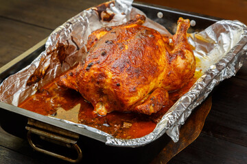 Whole baked chicken carcass with a crust in sauce on a foil on a baking sheet.