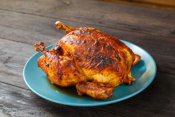 Whole baked chicken carcass stuffed with pears in soy sauce with a crispy crust on a blue plate.