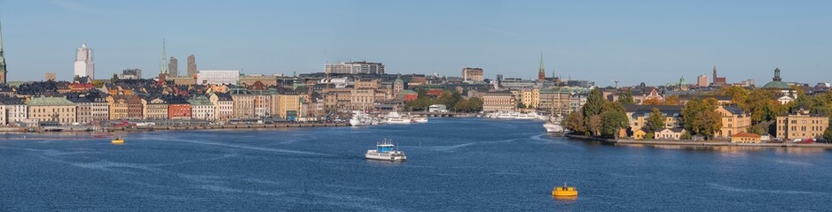 Fototapeta premium Panorama view over the bay Strömmen, the old town Gamla Stan with commuter boats, a harbor commuter ferry and a yellow anchor bollard a colorful sunny autumn day in Stockholm