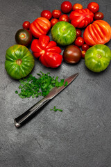 Different varieties of red and green tomatoes. Chopped parsley and knife.