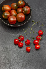 Fototapeta na wymiar Sprig of cherry tomato, red tomatoes in black bowl.