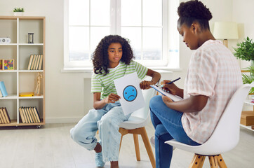 Psychologist working with stressed, unhappy child. Little African American school girl sitting on...