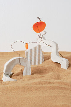 Vertical studio shot of modern installation of weird white gypsum objects, wire and plastic in sand, devastation concept