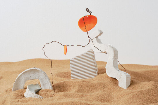 Horizontal close-up studio shot of creative composition of white gypsum objects, wire and plastic in sand, ruins concept