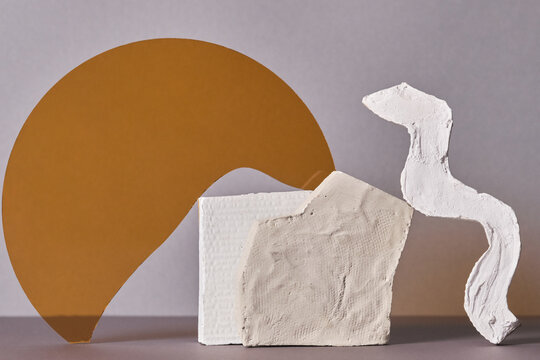 Horizontal close-up studio shot of contemporary still life installation of two white gypsum objects and yellow glass on gray background