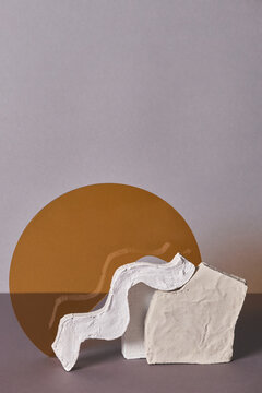 Vertical studio shot of trendy still life installation of two white gypsum objects and yellow glass on gray background