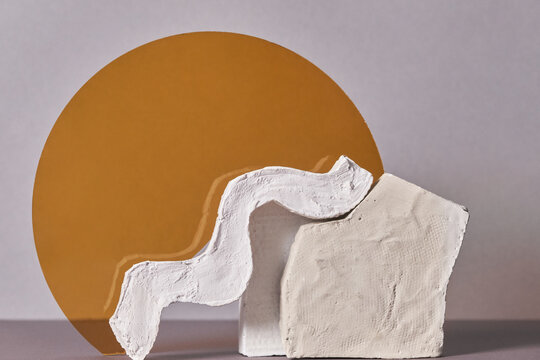 Horizontal close-up studio shot of contemporary still life installation of two unusual white gypsum objects and yellow glass on gray background