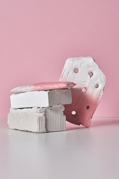 Vertical studio shot of trendy contemporary pink and white still life installation of gypsum objects on white table against pink wall background