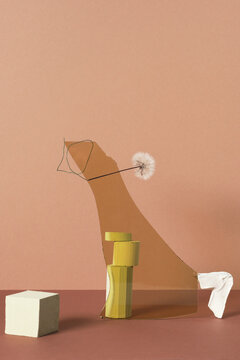 Vertical studio shot of balancing still life installation of gypsum and wooden objects, yellow glass and dandelion