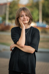 Portrait of a young beautiful fair-haired girl in dark clothes on the street of a summer city.