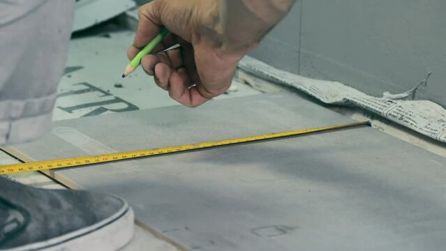 The master tiler transfers the dimensions from the wall to the tile for cutting holes for communications, using a tape measure pencil.