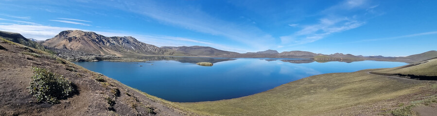 A beautiful landscape in Iceland of mountains, a bright blue and blue sky of light clouds, reflected in a huge flat surface of reservoir.